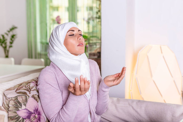 Jovem mulher rezando. Jovem muçulmana a rezar, dentro de casa. Jovem mulher muçulmana em hijab bege e roupas tradicionais rezando por Deus, espaço cópia. Árabe mulher muçulmana orando
 - Foto, Imagem