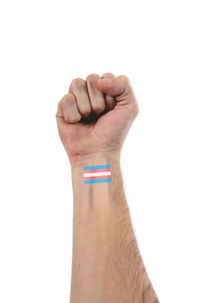Mooie en gestileerde hand en arm van blanke persoon met vuist omhoog en een kleine tatoeage van transgender vlag van trots meer dan 100% witte achtergrond - Foto, afbeelding