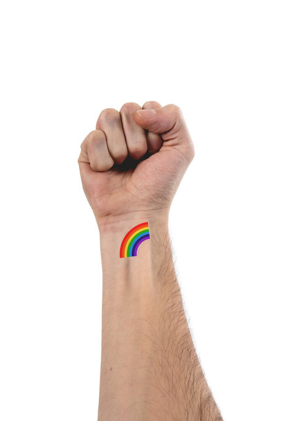 Beautiful and stylized hand and arm of caucasian person with fist up and a little tattoo of LGBTQ rainbow of pride over 100% white background - Foto, Bild