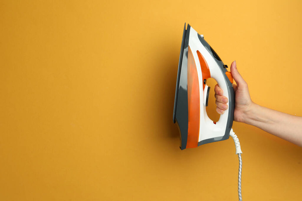Woman holding modern iron on orange background, closeup. Space for text - 写真・画像