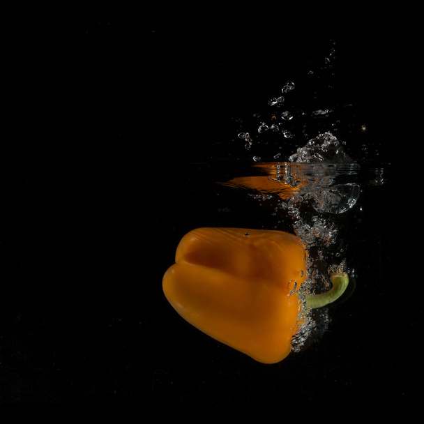 Orange Pepper Splashing Into Water On Black - Foto, afbeelding