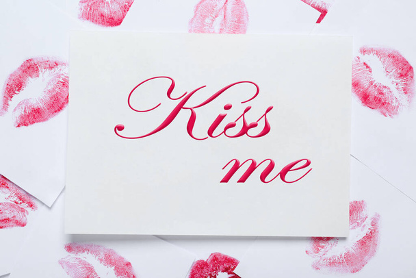 Card with phrase Kiss Me and lipstick marks on white background, top view - Фото, зображення