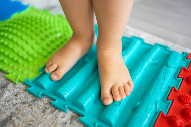 Close up view of Little girl walks on a massage mat. Toddler baby foot massage mat. Exercises for legs orthopedic massage carpet. . High quality photo - Photo, Image