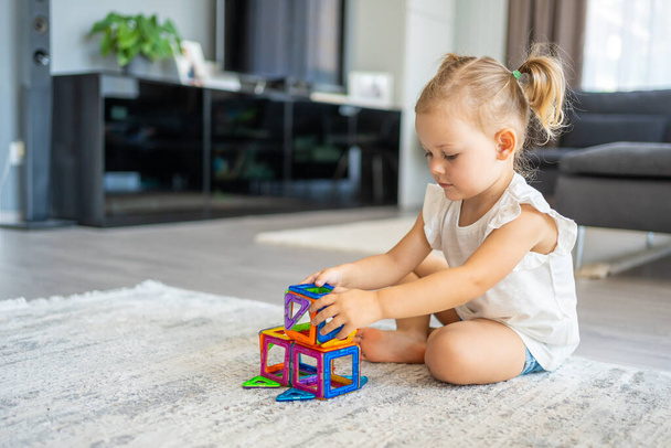 カラフルなマグネットプラスチックブロックキットを家庭で遊んでいる女の子。子供は教育ゲームをしている。幼児期の発達。高品質の写真 - 写真・画像