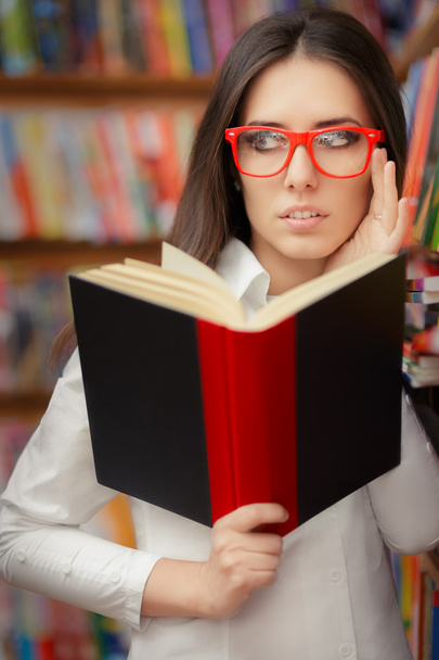 Young Woman with Glasses Reading Near Bookshelf - Zdjęcie, obraz