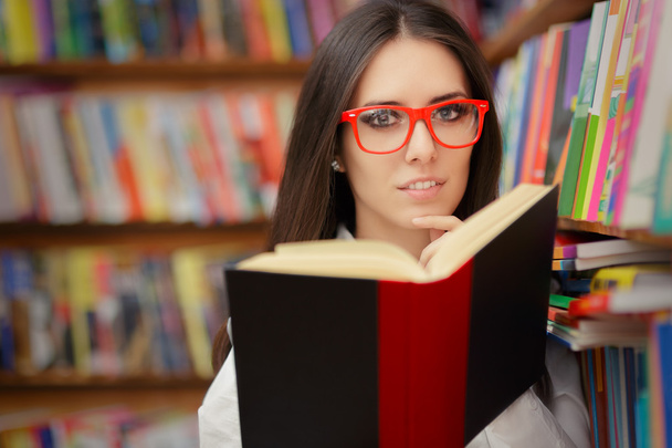 Young Woman with Glasses Reading Near Bookshelf - Foto, imagen