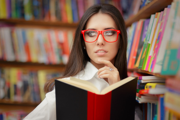 Young Woman with Glasses Reading Near Bookshelf - Fotoğraf, Görsel