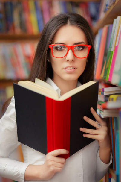 Young Woman with Glasses Reading Near Bookshelf - Fotó, kép