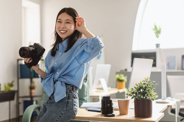 Digital Photography. Young Korean Female Photographer Holding Photocamera Smiling Looking At Camera Standing At Home. Creative Profession And Career Concept - Foto, Imagen