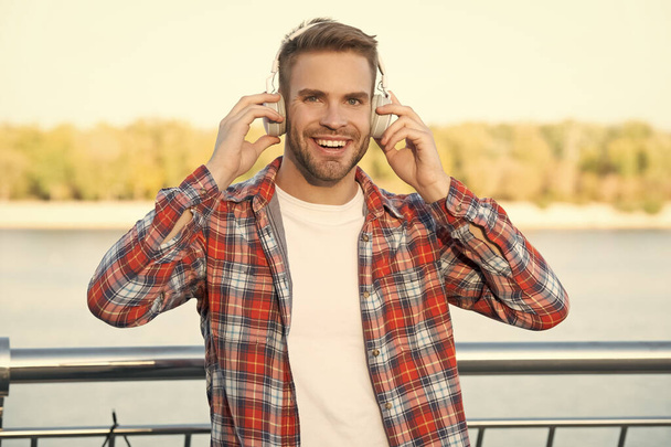 happy young bearded guy in checkered shirt and earphones outdoor, modern life. - Foto, imagen