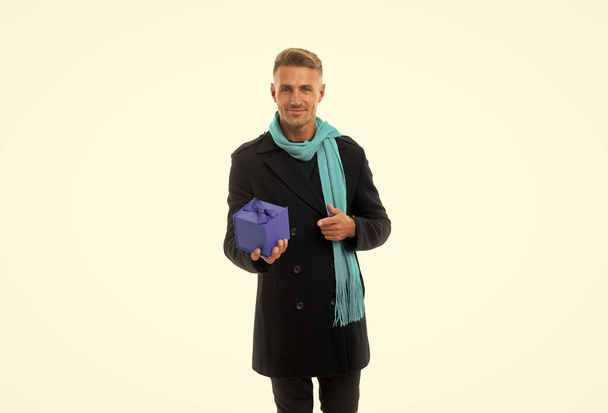 Happy handsome man in overcoat with long scarf pointing finger at present box isolated on white, gift. - Foto, immagini