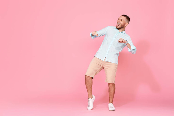 handsome smiling man in blue shirt dancing isolated on pastel pink background. Full length - Foto, imagen