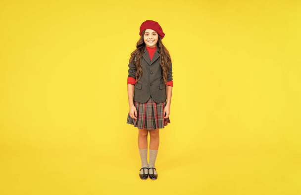 glücklich Teenager Mädchen in Uniform und Baskenmütze auf gelbem Hintergrund, Mode. - Foto, Bild