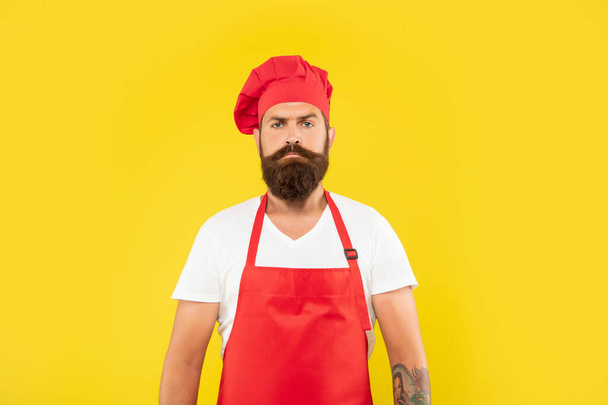 Serious man in red toque and apron yellow background, cook. - Fotografie, Obrázek