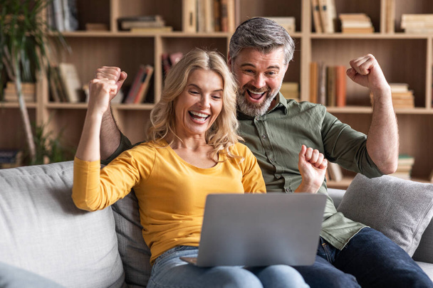 Online Win. Portrait Of Overjoyed Middle Aged Couple Celebrating Success With Laptop, Happy Cheerful Spouses Looking At Computer Screen, Raising Fists And Exclaiming With Excitement, Closeup - Foto, imagen
