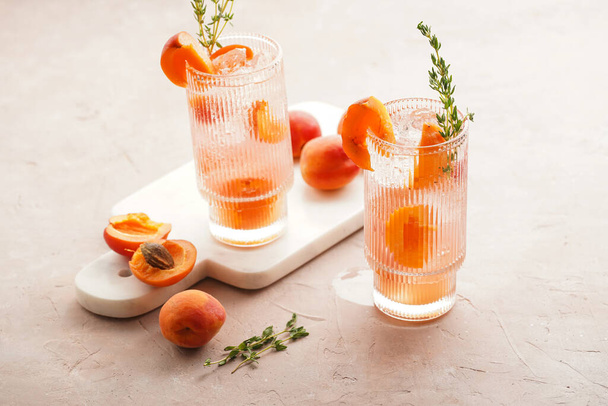 Two glasses with refreshing summer cocktail with ice cubes, apricot slices and fresh thyme on marble board on pale purple background - Foto, Imagem
