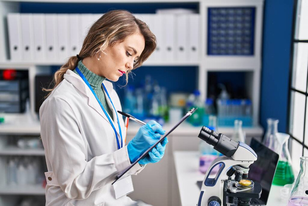Mujer joven científica escribiendo informe en laboratorio - Foto, Imagen