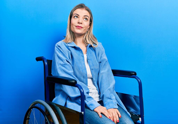Beautiful caucasian woman sitting on wheelchair smiling looking to the side and staring away thinking.  - Valokuva, kuva