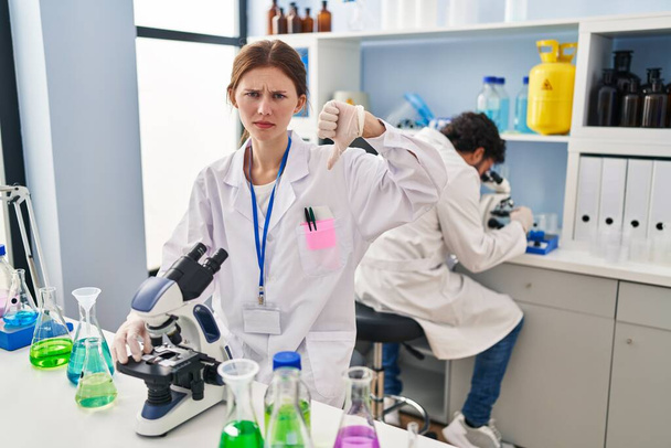 Young two people working at scientist laboratory with angry face, negative sign showing dislike with thumbs down, rejection concept  - Zdjęcie, obraz