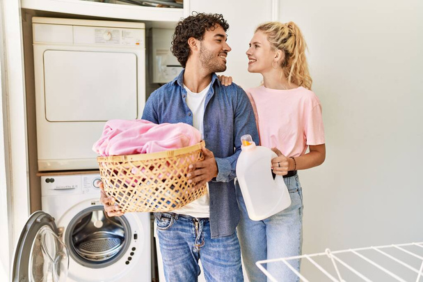 Genç çift evde çamaşır sepeti ve deterjan şişesiyle mutlu bir şekilde gülümsüyor.. - Fotoğraf, Görsel
