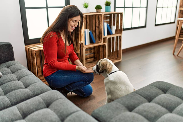 Joven mujer sonriendo seguro enseñando perro en casa - Foto, Imagen