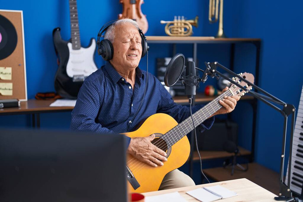 Senior grey-haired man musician singing song playing guitar at music studio - Fotó, kép