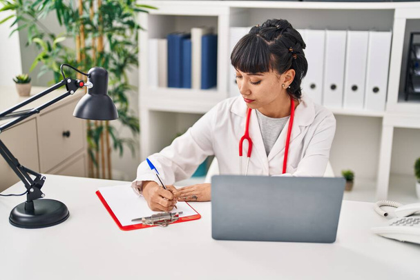Νεαρή γυναίκα που φοράει ιατρική στολή χρησιμοποιώντας φορητό υπολογιστή στην κλινική - Φωτογραφία, εικόνα