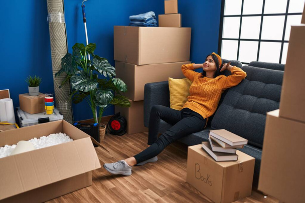Giovane donna latina rilassata con le mani sulla testa seduta sul divano in una nuova casa - Foto, immagini