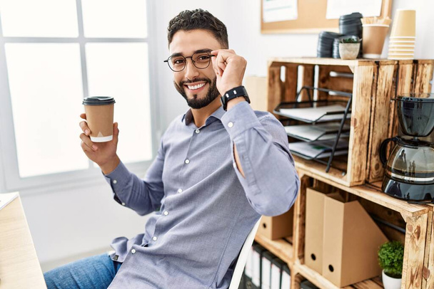 Молодой араб улыбается уверенно пьет кофе, работая в офисе - Фото, изображение