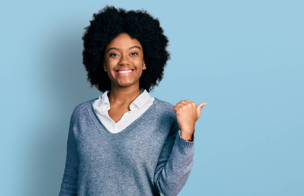 Joven mujer afroamericana vistiendo ropa de negocios sonriendo con la cara feliz mirando y señalando a un lado con el pulgar hacia arriba.  - Foto, Imagen