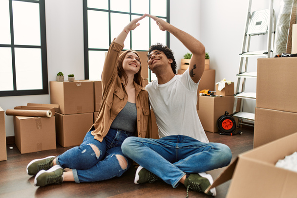 Mutlu bir şekilde gülümseyen genç çift yeni evlerinde elleri ile ev sembolü yapıyor.. - Fotoğraf, Görsel