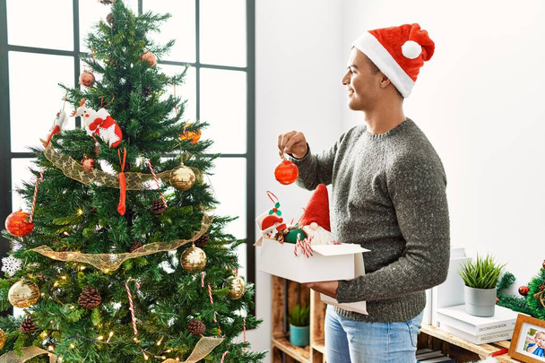 Mladý hispánec muž usměvavý sebevědomé zdobení vánoční stromek doma - Fotografie, Obrázek