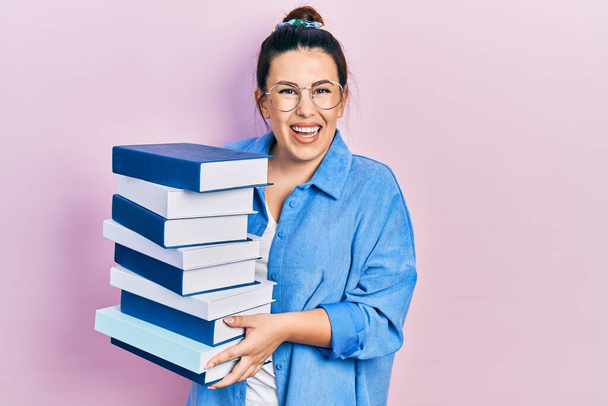 Young hispanic woman wearing glasses and holding books smiling with a happy and cool smile on face. showing teeth.  - Foto, imagen