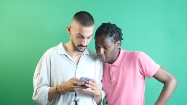 Kaksi miespuolista ystävää katsomassa hauskoja asioita puhelimessa, kuva tunteista ja kasvojen ilmeistä vihreän ruudun edessä - Materiaali, video
