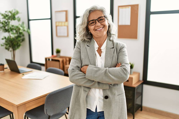 Middle age grey-haired businesswoman smiling happy standing with arms crossed gesture at the office. - Foto, immagini