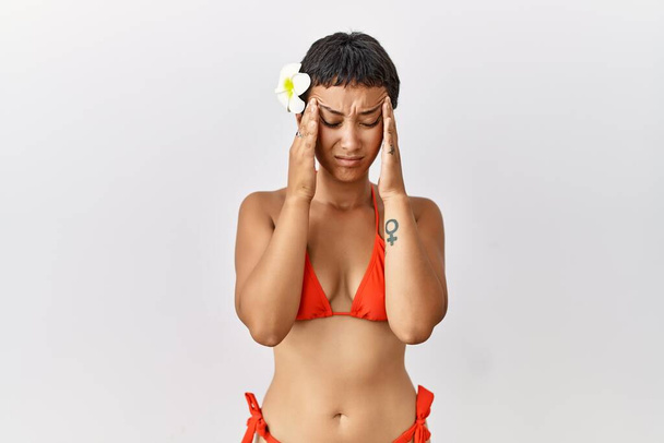 Young hispanic woman with short hair wearing bikini with hand on head, headache because stress. suffering migraine.  - Foto, Imagem