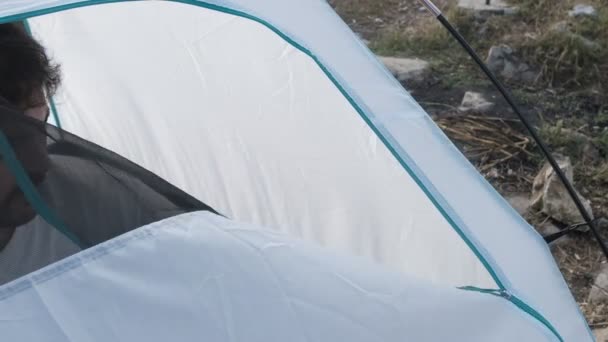 Camper opening tent, young vacationer male sleeping in tent, vacationer in white t-shirt staying in tent, unzipping the door of tent  - Filmati, video