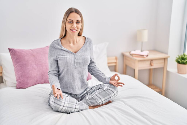 Mujer joven haciendo ejercicio de yoga sentada en la cama en el dormitorio - Foto, Imagen