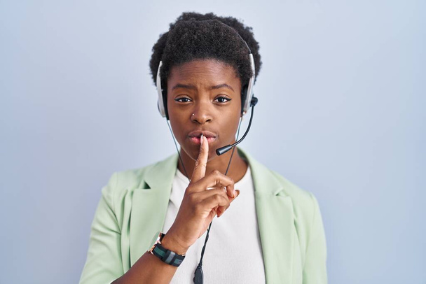 African american woman wearing call center agent headset asking to be quiet with finger on lips. silence and secret concept.  - Fotografie, Obrázek