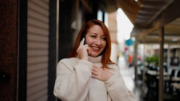 Mujer pelirroja joven sonriendo confiado hablando en el teléfono inteligente en la calle - Foto, imagen
