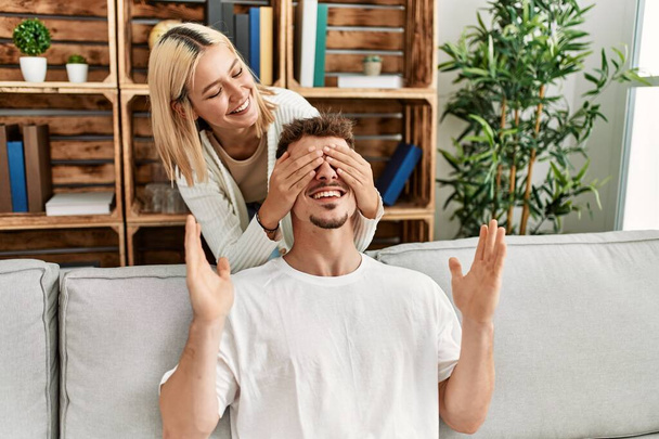 Woman surprising her boyfriend with hands on eyes at home. - Φωτογραφία, εικόνα
