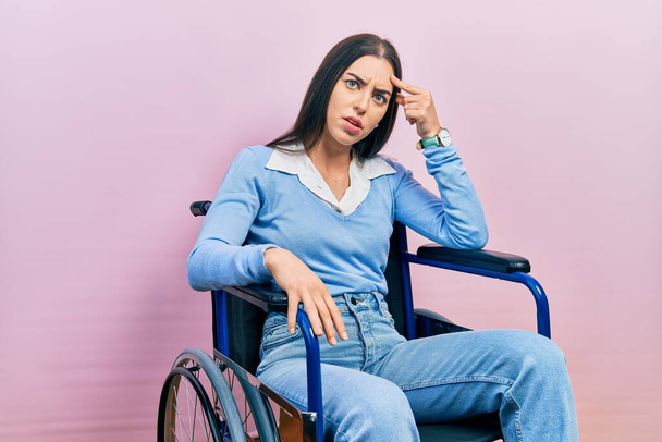 Красива жінка з блакитними очима, сидячи на інвалідному візку, вказуючи на нещасний прищик на лобі, потворну інфекцію чорноголових. проблеми з акне і шкірою
  - Фото, зображення