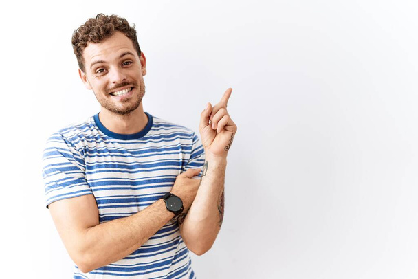 Handsome young man standing over isolated background with a big smile on face, pointing with hand finger to the side looking at the camera.  - Photo, Image