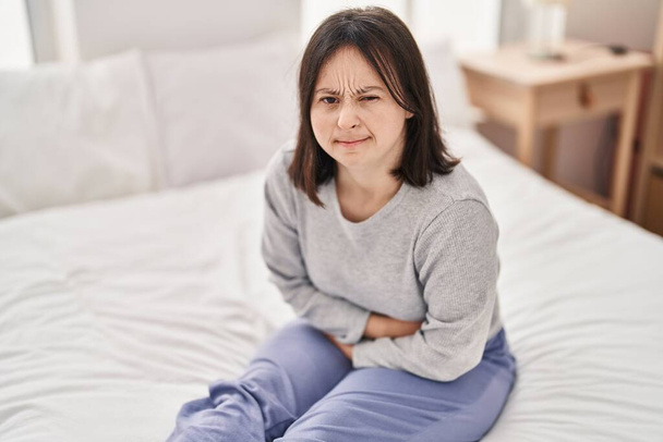Nuori nainen, jolla on alas oireyhtymä kärsii kuukautiskivusta istuu sängyssä makuuhuoneessa - Valokuva, kuva
