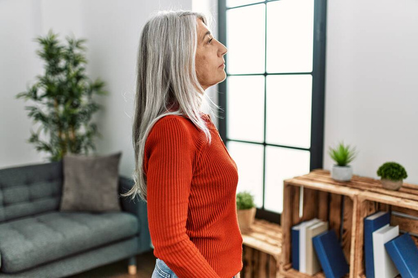 Middle age grey-haired woman wearing casual clothes standing at home looking to side, relax profile pose with natural face with confident smile.  - Foto, immagini