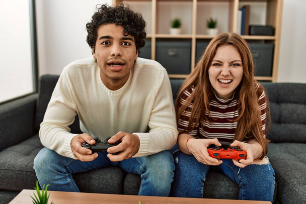 Νεαρό ζευγάρι με δυστυχισμένη έκφραση που παίζει βιντεοπαιχνίδι κάθεται στον καναπέ στο σπίτι. - Φωτογραφία, εικόνα