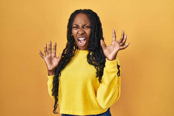 African woman standing over yellow background afraid and terrified with fear expression stop gesture with hands, shouting in shock. panic concept.  - Photo, Image