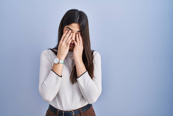 Young brunette woman standing over blue background rubbing eyes for fatigue and headache, sleepy and tired expression. vision problem  - Foto, afbeelding