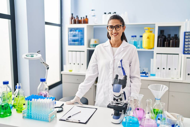 Laboratuvarda dikilen, bilim adamı üniforması giyen genç İspanyol kadın. - Fotoğraf, Görsel