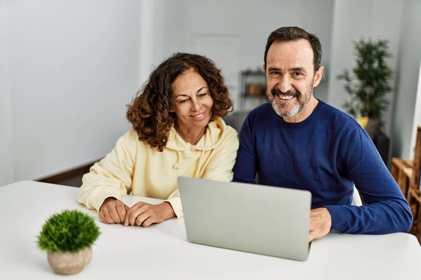 Middle age hispanic couple smiling happy using laptop at home. - 写真・画像